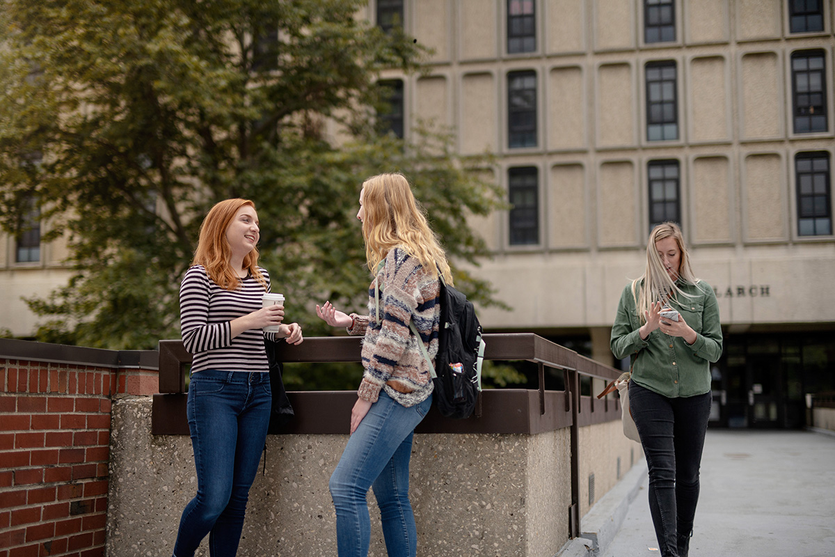 Students standing outside of Maple Hall chatting and drinking coffee