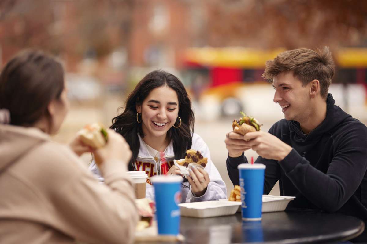 Three students eating sandwiches and talking together outdoors