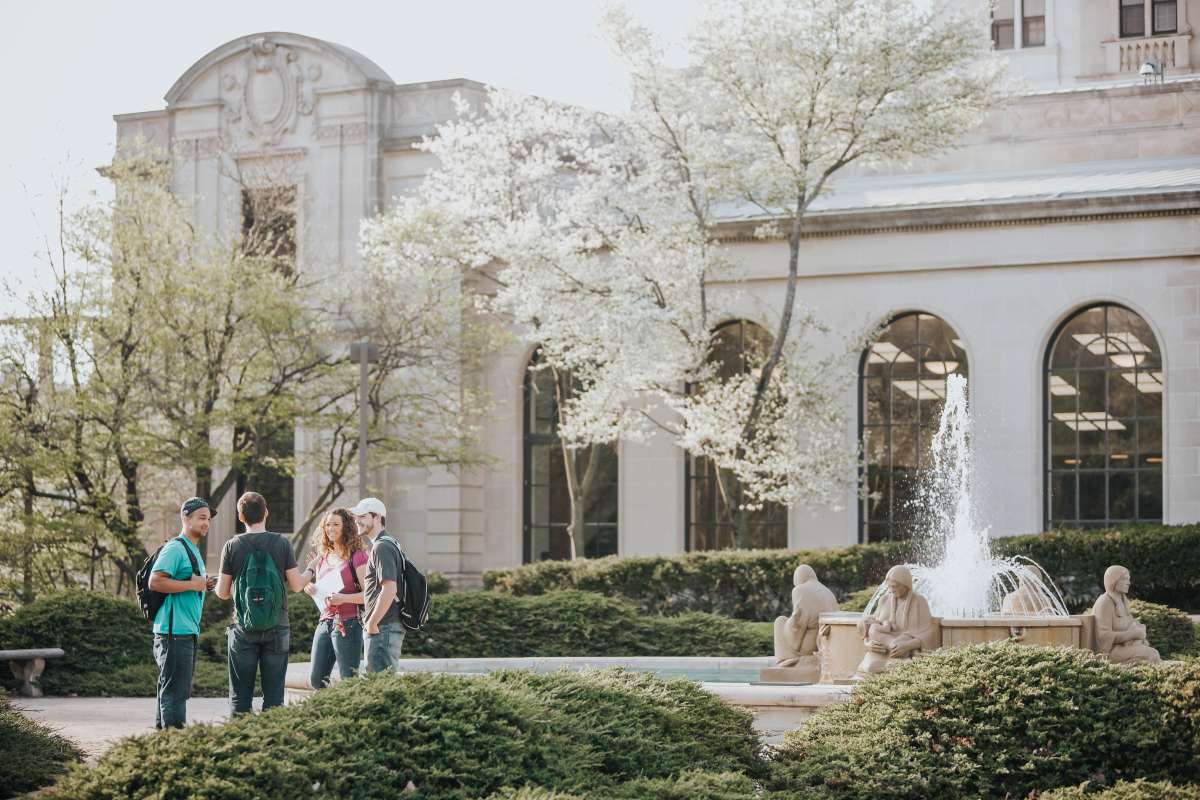 A group of four students stands and talks nearby the Four Seasons Fountain on the north side of the Memorial Union.