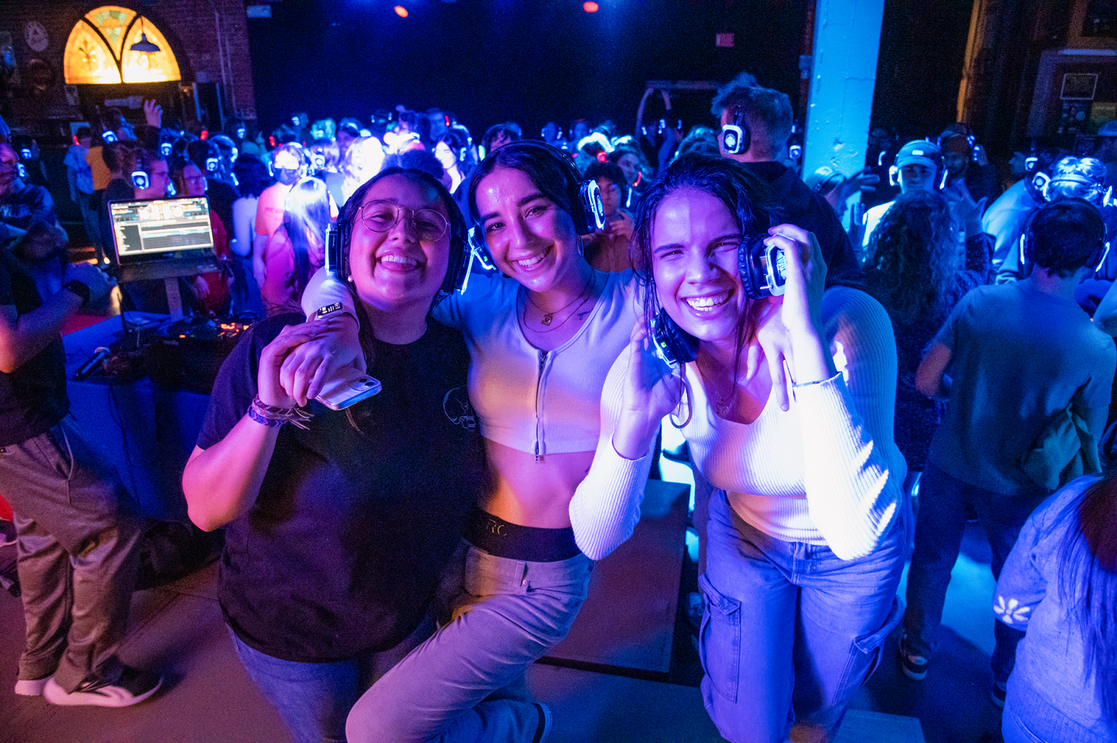 A group of students poses in the Maintenance Shop under dark lighting for a silent disco event.